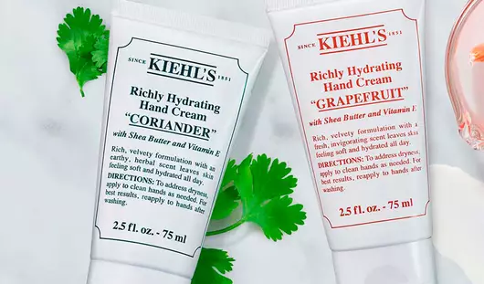 Hautpflegeprodukte von Kiehl's auf einem marmorierten Tisch, einschließlich einer Creme in einer Tube und frischen Fruchten.