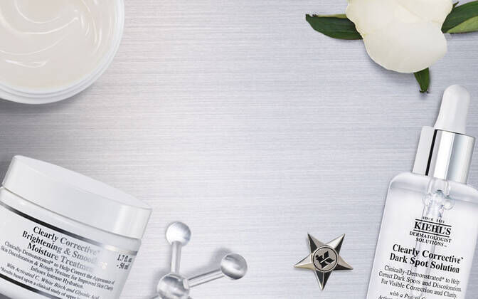 Alt-Text: Eine flache Ansicht von Kiehl's Hautpflegeprodukten auf einer silbernen Oberflache, umgeben von Blumen und einem Glasbehalter.