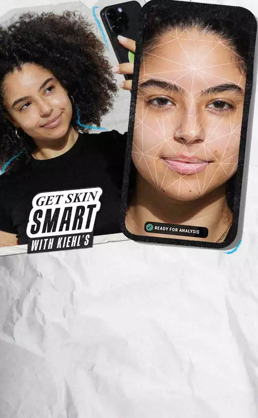 Eine Frau mit lockigem Haar schaut lachelnd, wahrend sie ein Smartphone in der Hand halt, das ein Hautanalyse-Overlay zeigt. In der Ecke steht der Text "GET SKIN SMART WITH KIEHL'S".