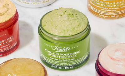 Grune Avocado-Nahrungshydrationsmaske von Kiehl's, umgeben von verschiedenen anderen Hautpflegeprodukten auf einem Marmoruntergrund.