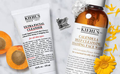 Kiehls Gesichtsreiniger: Ultra Facial Cleanser und Calendula Deep Cleansing Face Wash, umgeben von Bluten und Fruchten.