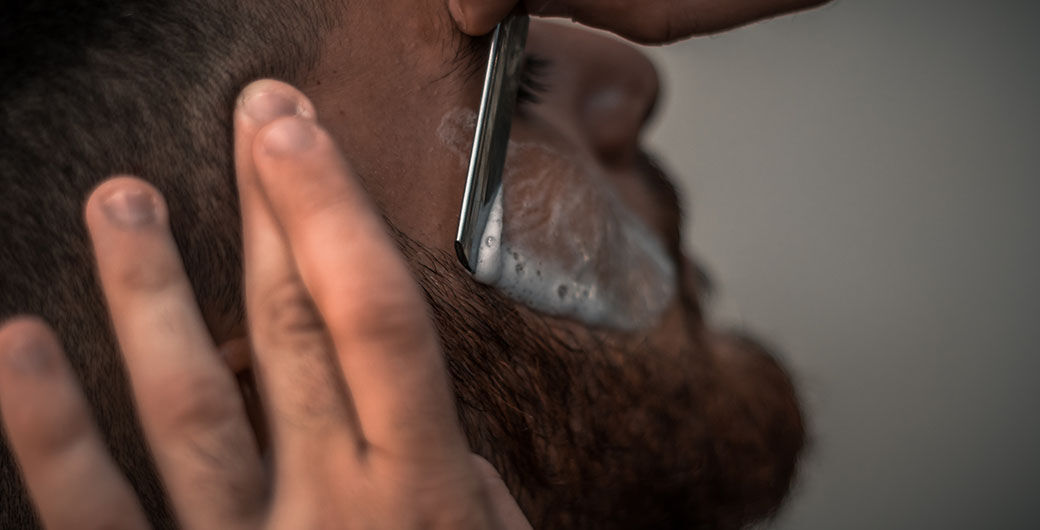 Rasierer an Bart auf grauem Hintergrund