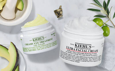 Zwei Kiehl's Hautpflegecremes: Avocado-Augenbehandlung und Ultra Gesichtscreme, umgeben von Avocado und Oliven.