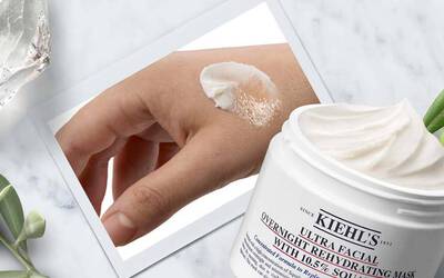 Eine Hand mit Kiehl's Ultra Facial Overnight Maske, daneben die offene Produktverpackung vor einem neutralen Hintergrund.