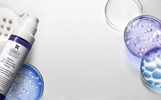 Bild mit verschiedenen Laborglasern und einer Flasche Hautpflegeprodukt, umgeben von transparenten Gel-Texturen.