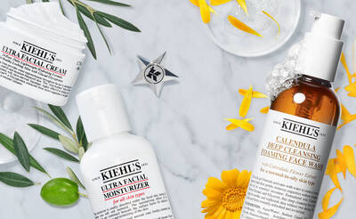 Kiehls Produkte: Gesichtscreme, Feuchtigkeitscreme und Reinigungsschaum auf marmoriertem Hintergrund mit Blumen.