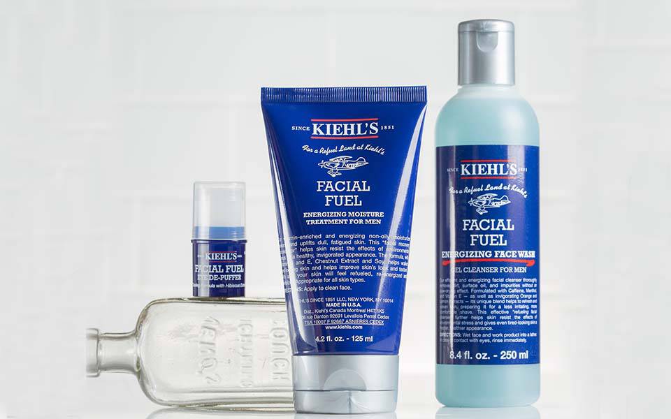 Ein Banner mit Kiehl's Gesichtsprodukten, darunter eine Flasche, eine Tube und ein Tiegel, vor einem hellen, marmorierten Hintergrund.