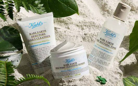 Alt-Text: Ein marmorierter Hintergrund mit einer Tube Gesichtscreme, einem offenen Tiegel Lotion und einigen naturlichen Inhaltsstoffen, wie gruner Minze und Pulver.