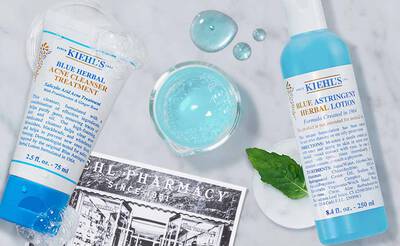 Zwei Kiehl's Produkte fur die Hautpflege: blauer Gesichtsreiniger und astringierende Lotion, umgeben von Wassertropfen.