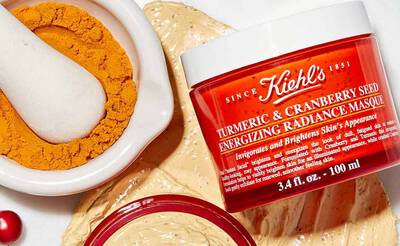 Kiehl's Gesichtsmaske mit Kurkuma und Cranberry, umgeben von Kurkumapulver und einer cremigen Textur.