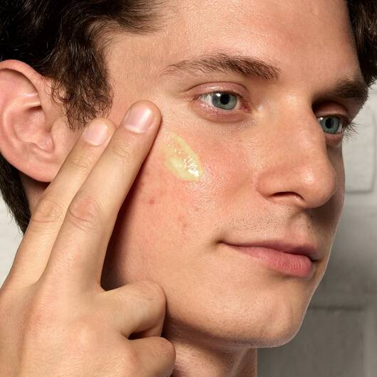 Gesicht eines jungen Mannes, der ein Retinol Serum mit zwei Fingern auf seine Wange auftragt