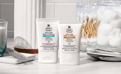 Zwei Kiehl's Sonnencremes auf einem Tisch, umgeben von Kosmetik-Utensilien und Baumwollprodukten.