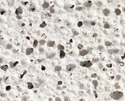 Close-up of a porous, white surface with numerous small holes and an uneven texture.