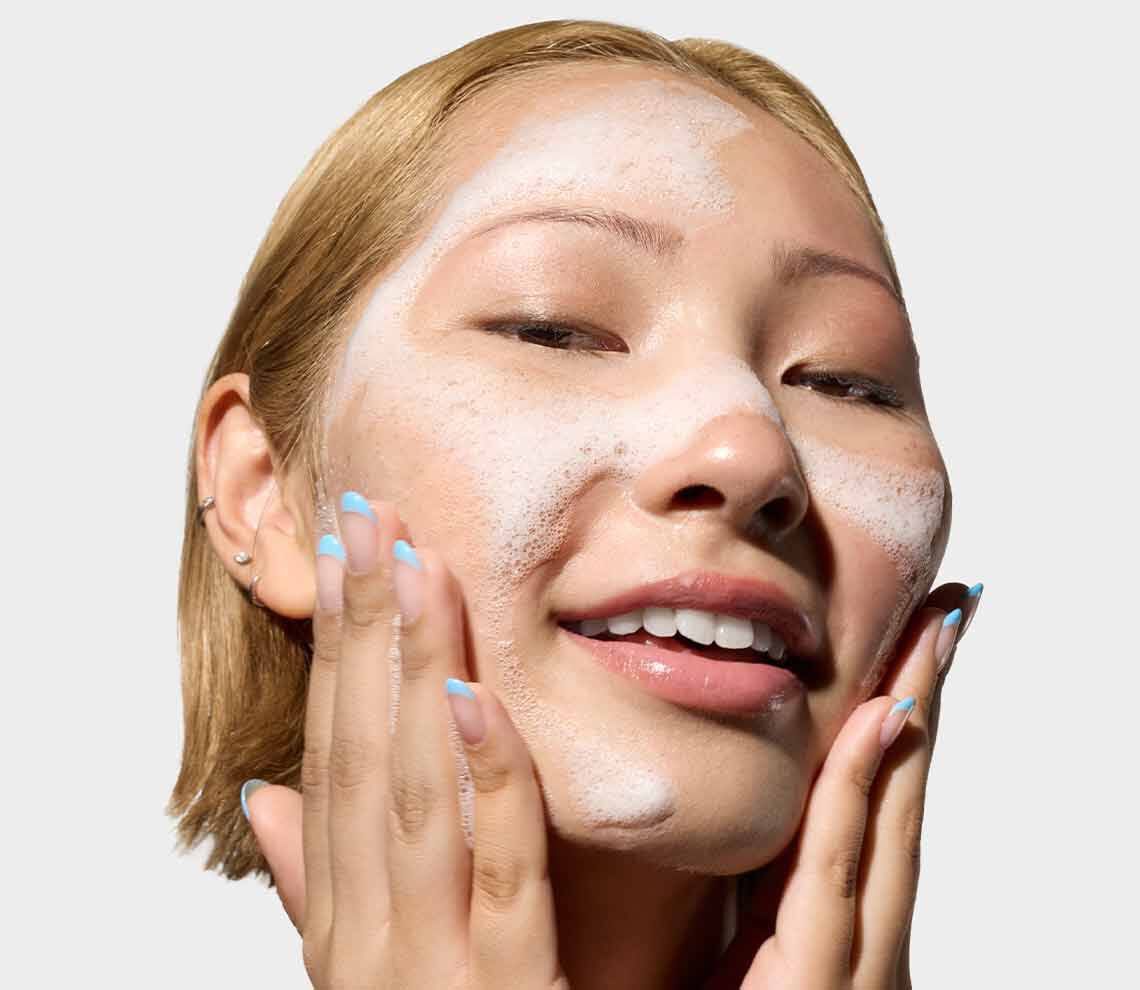 Flaschen mit Kiehl’s Hautpflegeprodukten mit Vitamin C vor einem Hintergrund aus Orangen und Orangenscheiben