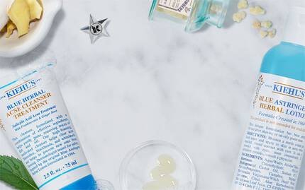 Eine Anordnung von Kiehl's Hautpflegeprodukten auf einer marmorierten Flache, umgeben von frischen Zutaten wie Minze und Ingwer.