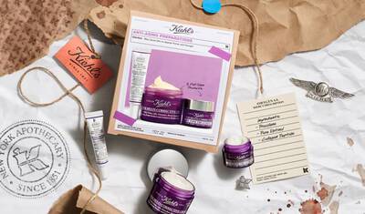 A flat lay image featuring Kiehl's anti-aging products, including a cream jar and a serum, arranged on crumpled paper with various textures and a vintage aesthetic.