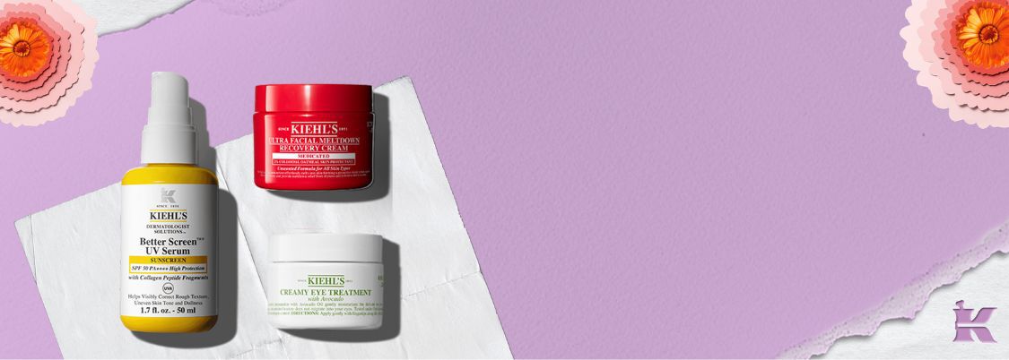 Werbebanner von Kiehl's auf hellviolettem Hintergrund mit Papierblumen-Dekoration, der drei Produkte prasentiert: Better Screen UV Serum SPF 50 PA++++ mit Kollagen-Peptid-Fragmenten (50 ml), Ultra Facial Meltdown Recovery Cream (medizinische Formel mit 1% kolloidalem Hafer) und Creamy Eye Treatment with Avocado.
