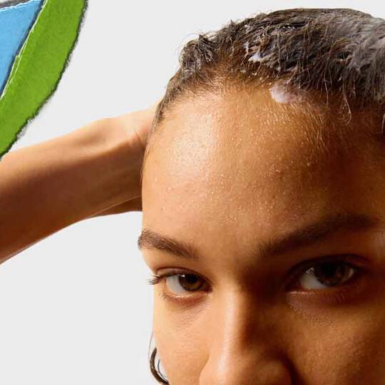 Eine Person mit nassem Haar tragt ein Haarprodukt auf, im Hintergrund ein farbenfroher Abschnitt aus gerissenem Papier.