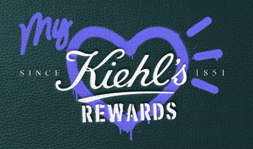 „My Kiehl’s Rewards“-Logo mit einem lila Herz auf einem grun strukturierten Hintergrund.